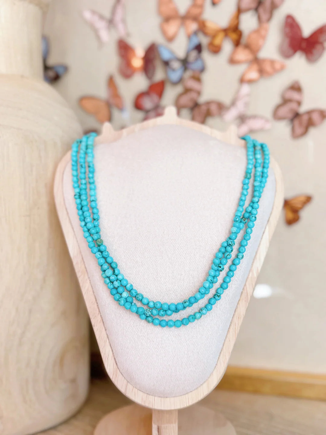 Turquoise beaded necklace on a mannequin bust with a butterfly-themed background