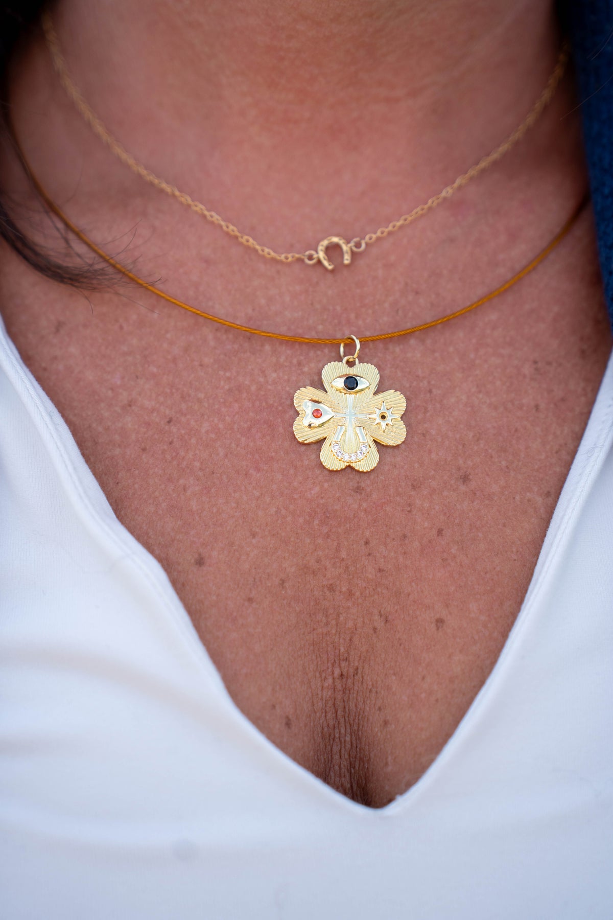 A close-up of a person's neck and chest wearing two layered necklaces. The top necklace is a delicate gold chain with a small crescent moon pendant.